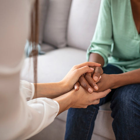 Two people holding hands on a couch, symbolizing support and connection.