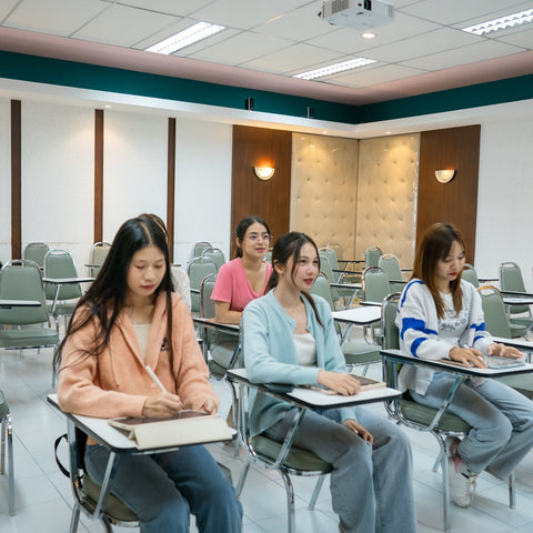 Small group of college-aged students seated in a classroom taking notes while an instructor stands at the front, representing early academic engagement and learning support.
