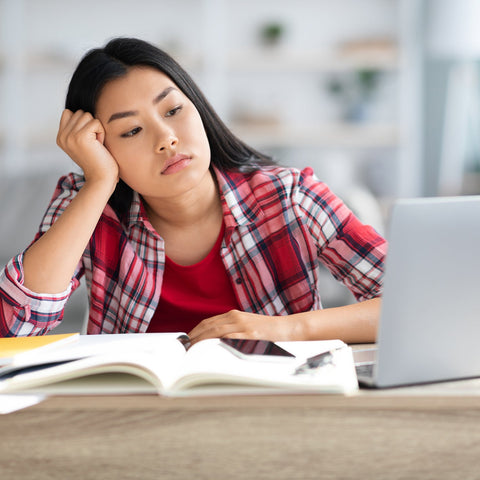 Woman sitting at a desk with a laptop and books, looking tired.