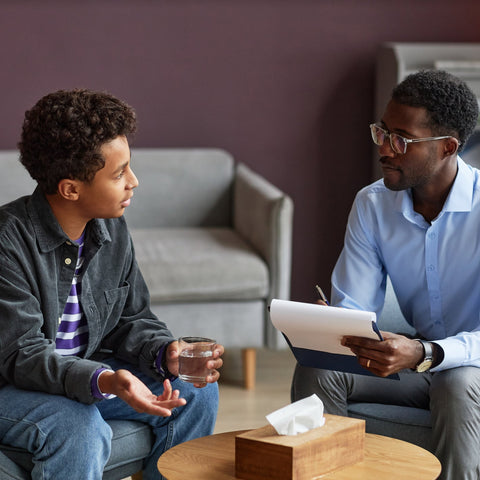 A young man talks with a counselor taking notes during a supportive one-on-one counseling session.