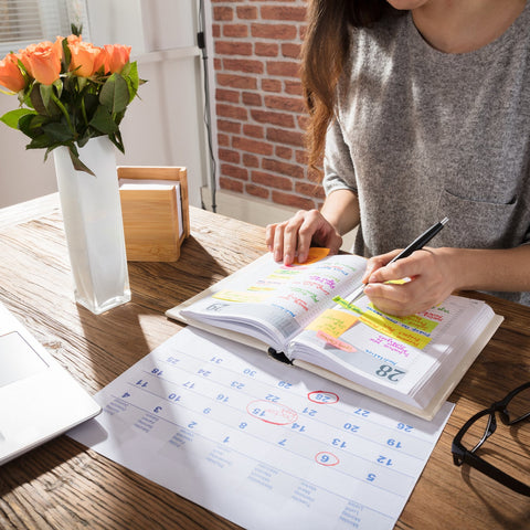 Person sitting at a desk with a laptop, books, and a vase of flowers.