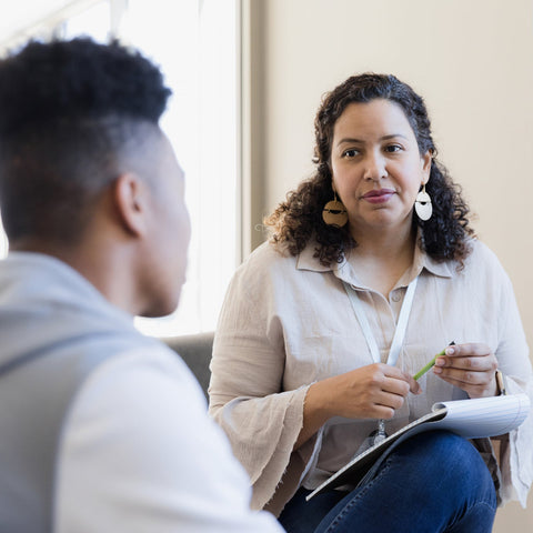 Woman in a professional setting holding a pen and clipboard, engaged in conversation with another person.