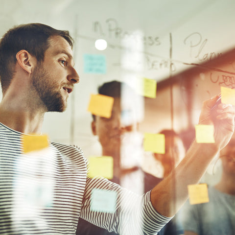 Two people working together on a glass board with sticky notes in an office setting.