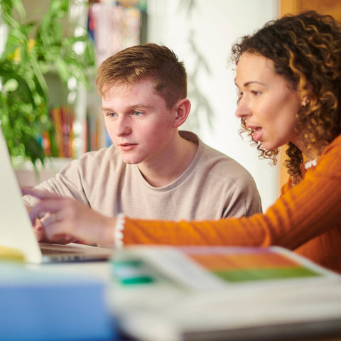 A female tutoring a male student sitting at a table