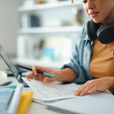 Person working at a desk with a laptop and documents, wearing headphones and a smartwatch.