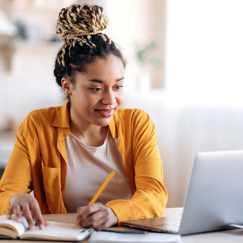 College student studying at home, using a laptop and taking notes in a notebook, representing career planning, learning, and preparation for future goals.