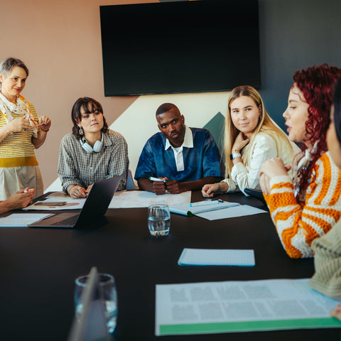 Group of people in a meeting around a table with documents and a laptop.