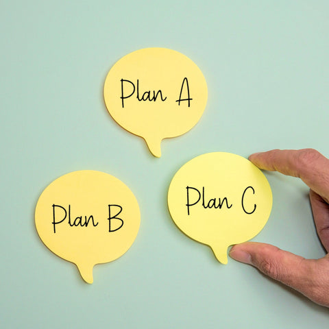 Hand placing yellow speech bubble cards labeled 'Plan A', 'Plan B', and 'Plan C' on a light blue background.