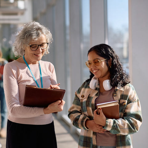 Two women in a college setting, one holding a folder and the other a notebook