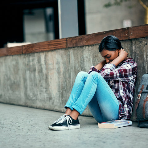 Person sitting on a concrete ledge with a backpack and book, appearing stressed.