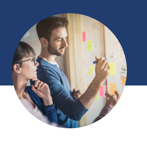 Two people writing and brainstorming on a whiteboard covered in colorful sticky notes.