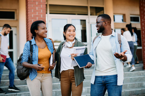 Three students standing on a school staircase, smiling and engaged in conversation.