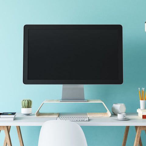 Modern office desk with computer monitor, office supplies, and a light blue wall.