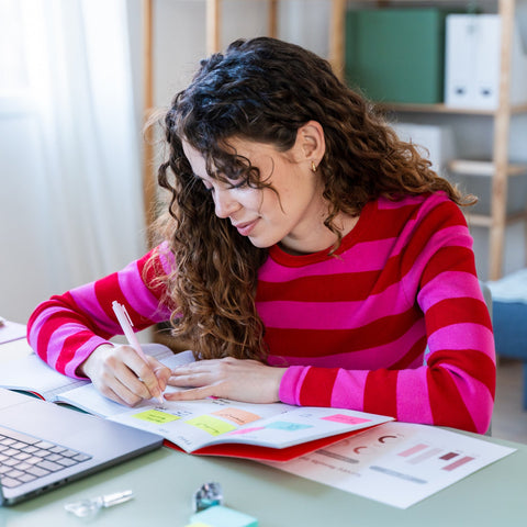 Student using color-coded sticky notes and a notebook to organize study materials at her desk.