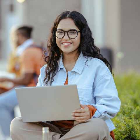 Woman holding a laptop outdoors, smiling at the camera