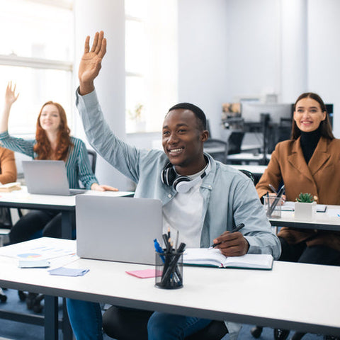 Diverse group of college students in a classroom raising their hands and participating in discussion, representing engagement, inclusion, and active learning.
