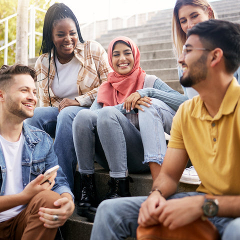 Group of young adults sitting on steps outdoors, smiling and interacting.