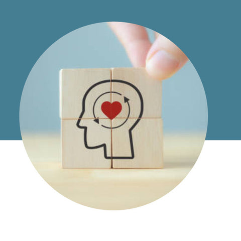 Wooden block with a drawing of a head with a heart and an arrow, held by a hand against a blue background.