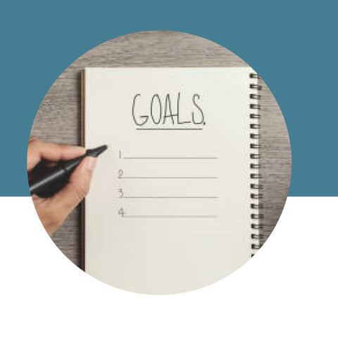 Notebook with 'GOALS' written on it, held by a hand with a pen, against a blue background.