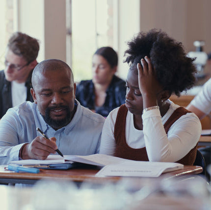 Teacher assisting a student with coursework in a classroom.
