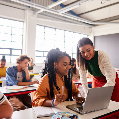 Teacher assisting a student with a laptop in a classroom setting