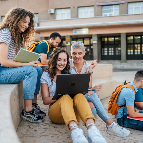 Group of students sitting outdoors with a laptop and books