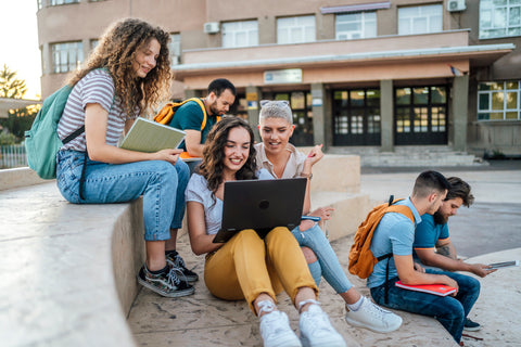Group of students sitting outdoors with a laptop and books