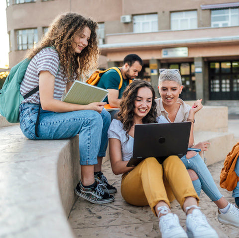 Group of students sitting outdoors with a laptop and books