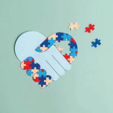 Two hands shaking in a heart shape made of colorful puzzle pieces on a green background.