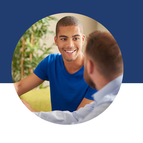 Two men talking closely, one smiling and gesturing toward the other.