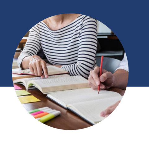 Two people reviewing open books together at a table with colorful sticky notes.
