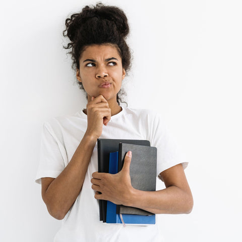 Thoughtful college student holding notebooks, looking to the side with a contemplative expression against a neutral background.