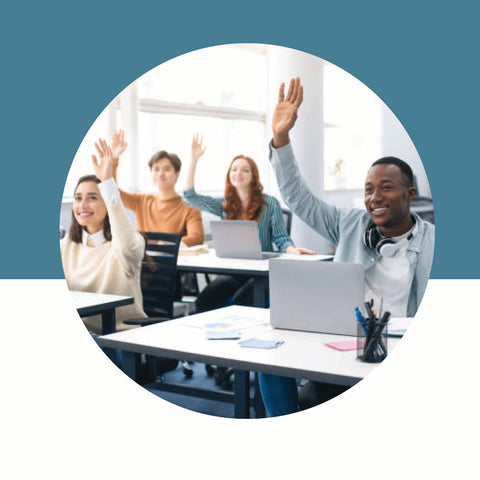 Students in a classroom raising hands while using laptops