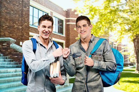 Two smiling college students fist bumping outside a campus building with backpacks and books.