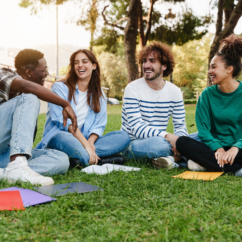 Four friends sitting on grass in a park, smiling and enjoying each other's company.