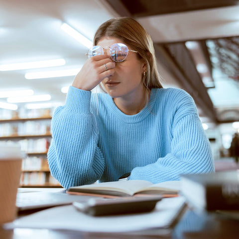 Woman in a library with books and a coffee cup, appearing stressed.
