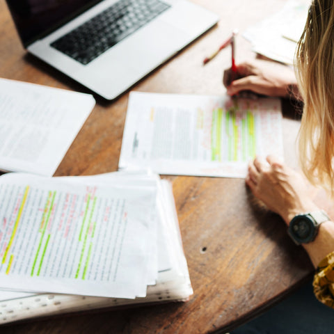 Person grading papers at a desk with books, a laptop, and a coffee mug.