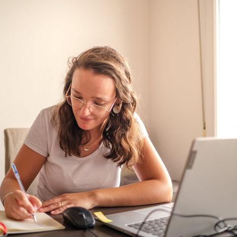 Woman sitting at a desk with a laptop, notebook, and pen, working or studying.