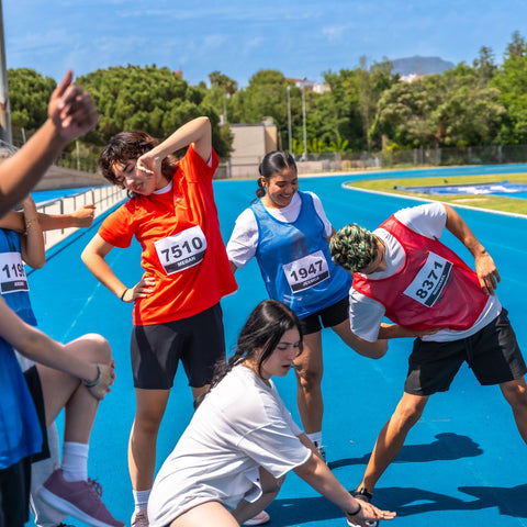 Group of people participating in a race or physical activity on a blue track with trees in the background.