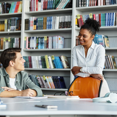 Two people sitting at a table in a library with bookshelves in the background