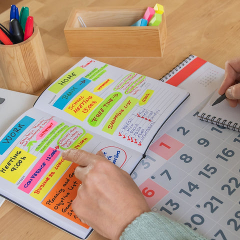 Person using a planner with colorful sticky notes on a desk with a laptop and stationery.