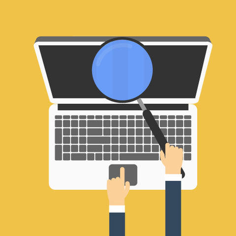 A person holding a magnifying glass over a laptop keyboard, with one finger pointing at the touchpad.