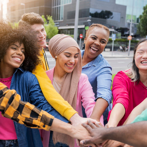 Group of people with diverse backgrounds holding hands outdoors.