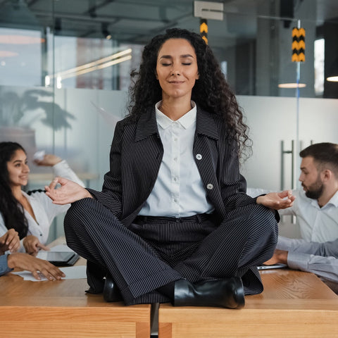 Woman meditating in an office setting with colleagues around