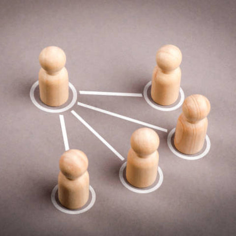 Five wooden peg figures connected by lines on a gray surface, representing a network of people.