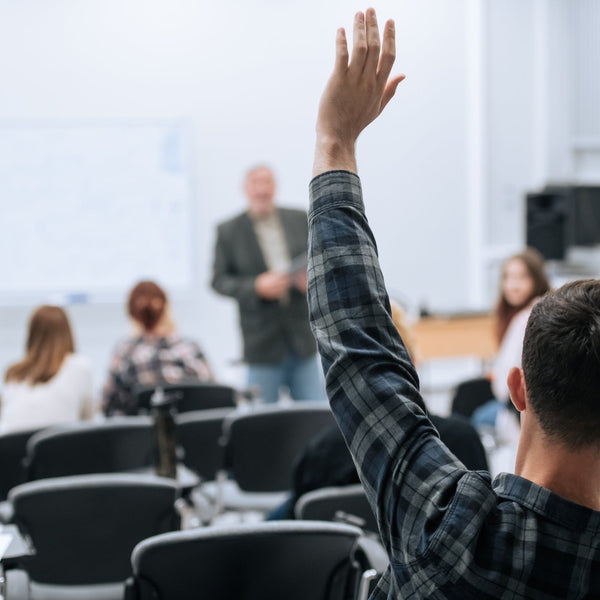 Person raising hand in a classroom setting with other students and a lecturer.