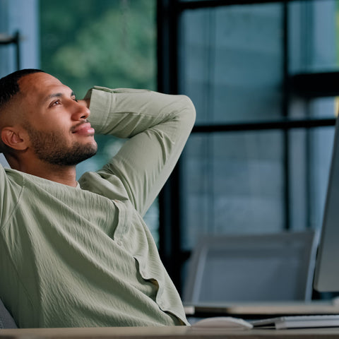 Man sitting at a desk with his hands behind his head in an office setting