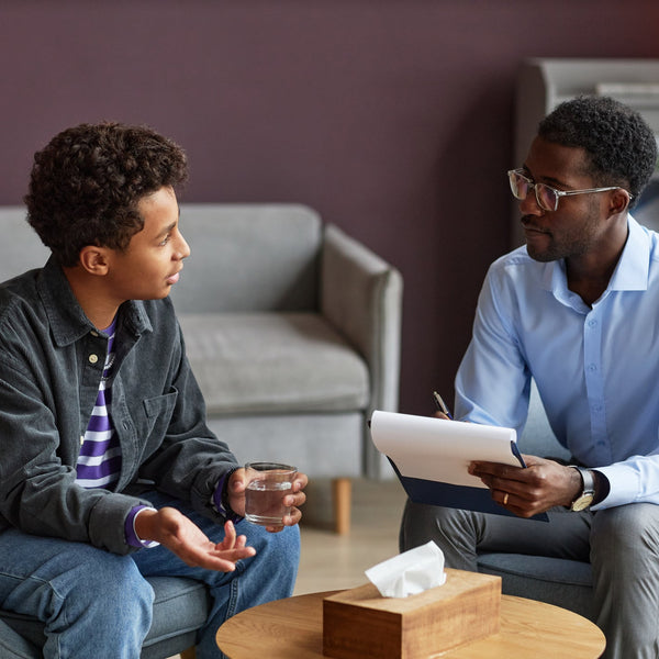 A young man talks with a counselor taking notes during a supportive one-on-one counseling session.