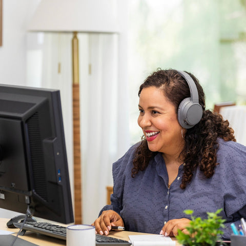 Woman wearing headphones sitting at a desk with a computer, smiling.
