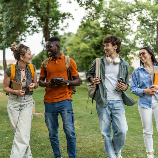 Four students walking outdoors in a park, engaged in conversation.